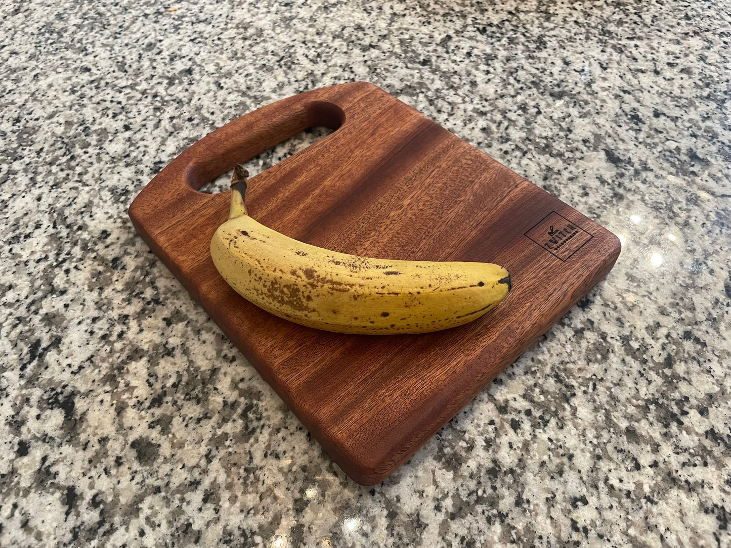 Banana on a wooden cutting board with 'Zwitch Woodworking' branding on a granite countertop.
