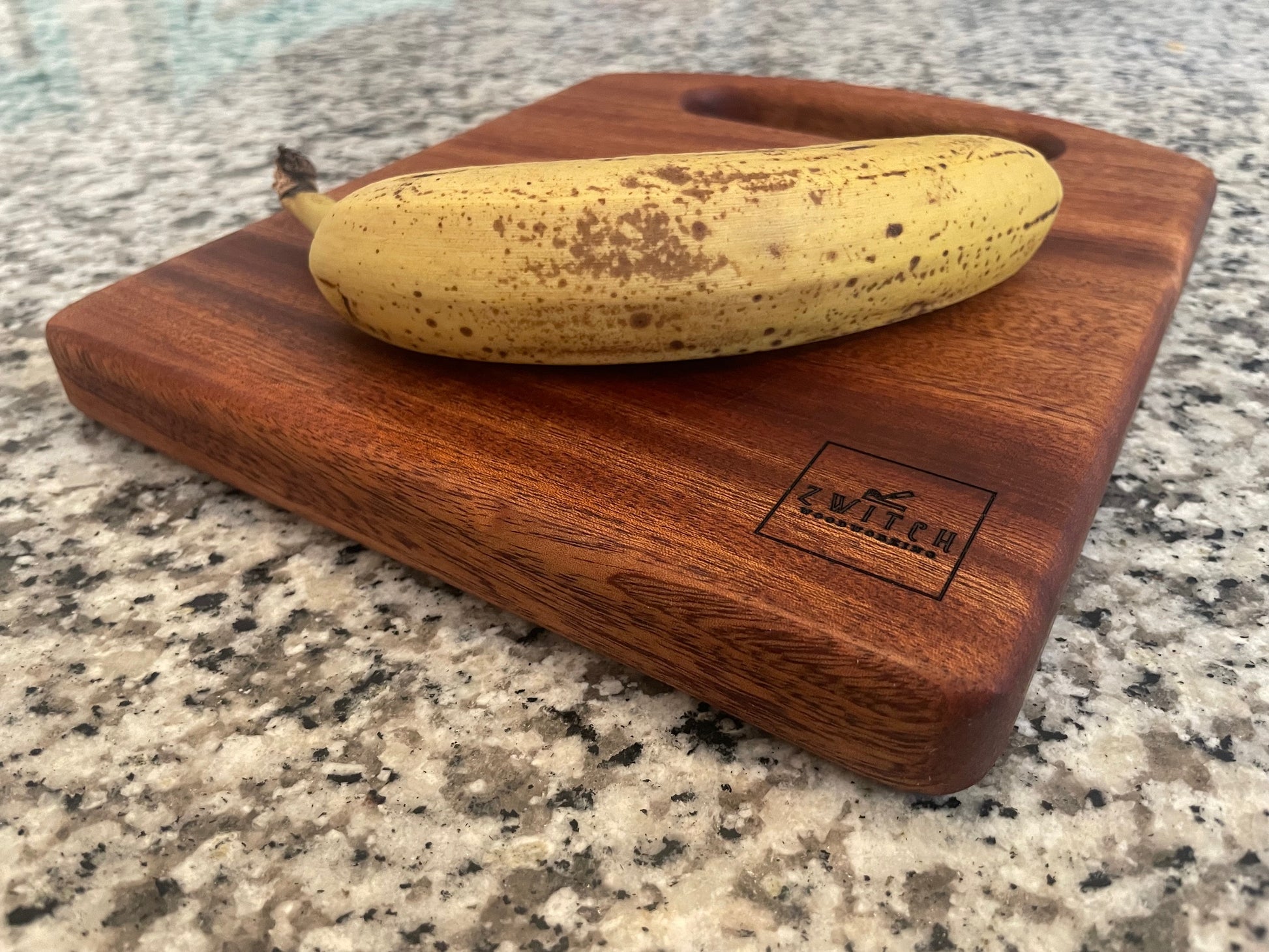 Wooden cutting board with a banana on a granite countertop